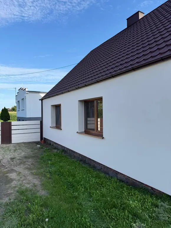 Elewacja boczna po ociepleniu — gładki biały tynk i osadzona stolarka okienna