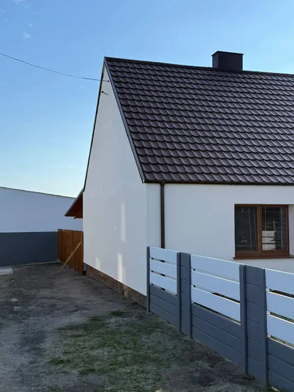 Ten sam szczyt budynku po ociepleniu — równy biały tynk, wykończone narożniki i rynna